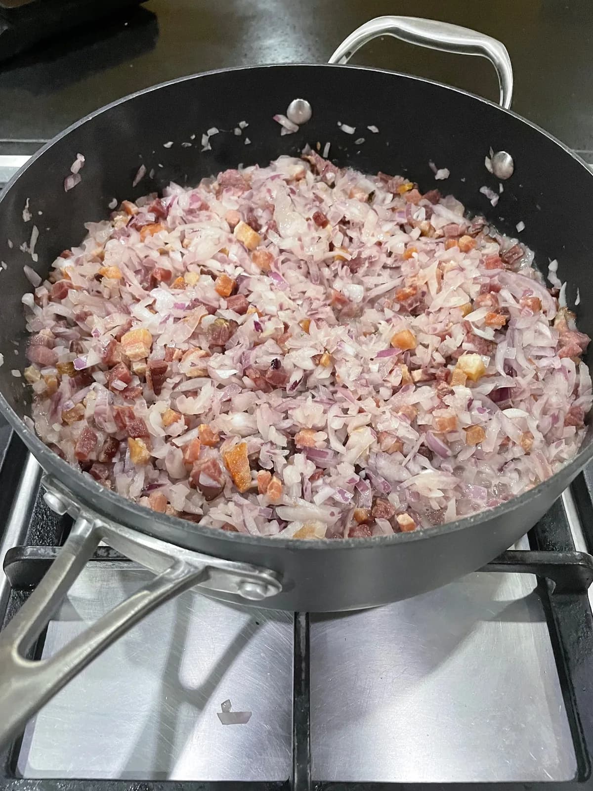 Chopped onions covering small pieces of smoked bacon trimmings in a large pan at the start of making bacon jam